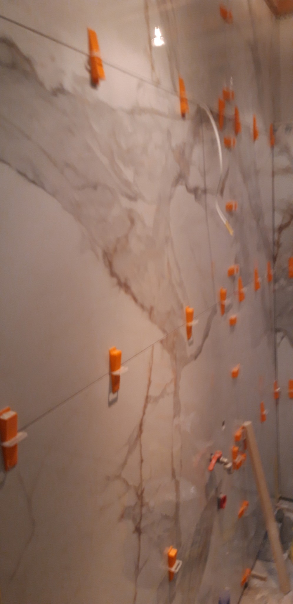 Montaż płytek imitujących marmur na ścianie z użyciem poziomicy laserowej i klipsów poziomujących w trakcie prac wykończeniowych.