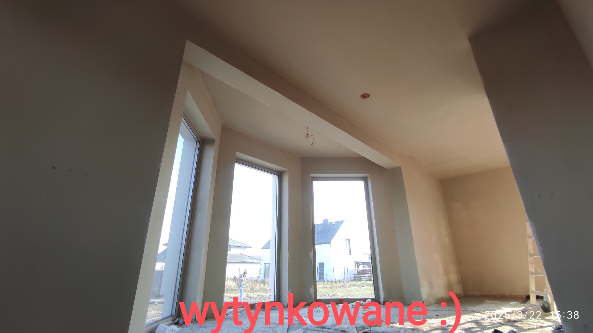 Wnętrze poddasza z trzema oknami po wykonanych pracach wykończeniowych ścian i sufitu, widoczne ślady po taśmach malarskich na podłodze.
