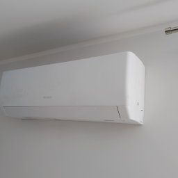 KLIMACIK ADRIAN WOJCIECHOWSKI - Biały klimatyzator marki Gree zamontowany na jasnej ścianie, widoczny fragment sufitu i karnisza. Minimalistyczny design.