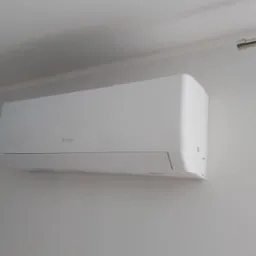 Biały klimatyzator marki Gree zamontowany na jasnej ścianie, widoczny fragment sufitu i karnisza. Minimalistyczny design.