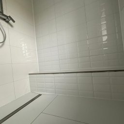 Usługi Remontowo-Budowlane DANIEL SOKOŁOWSKI-RYCHLIŃSKI - Nowoczesna kabina prysznicowa z białymi, błyszczącymi płytkami typu metro, szara podłoga z odpływem liniowym i chromowana armatura.