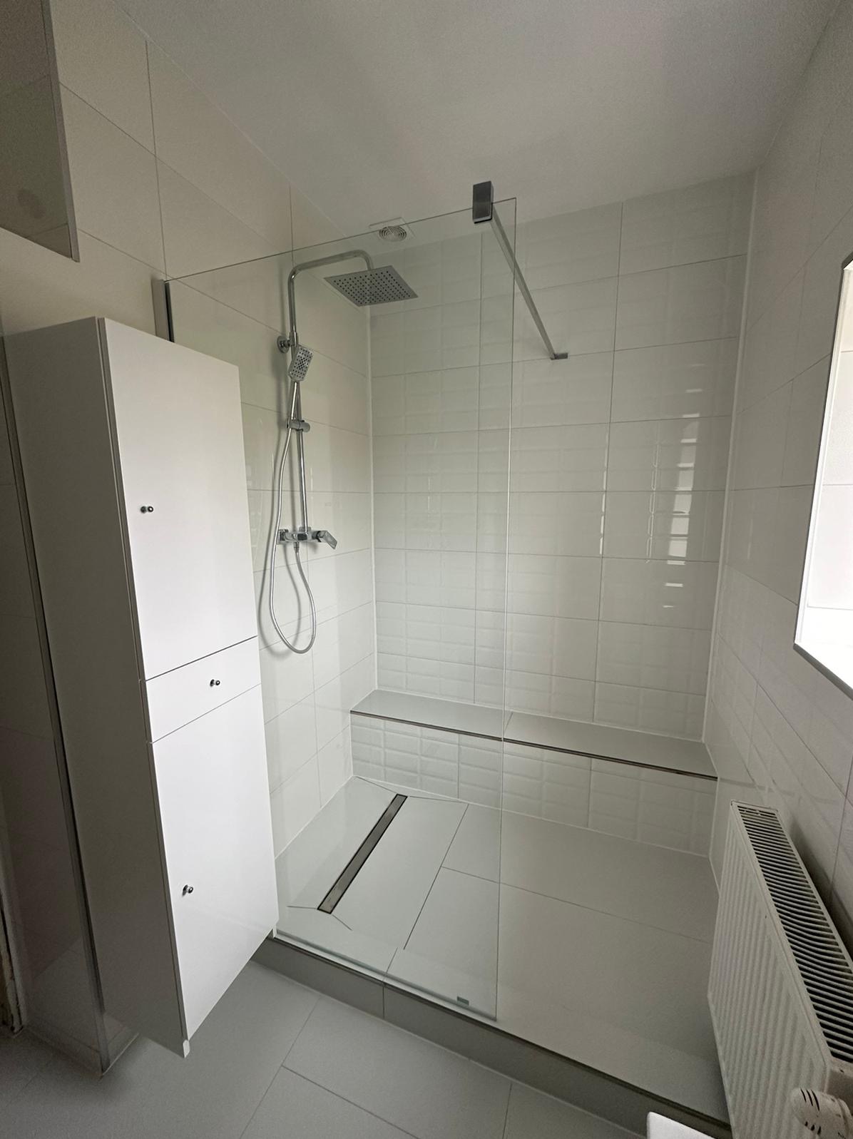 Nowoczesna kabina prysznicowa walk-in z odpływem liniowym, białe płytki imitujące cegłę i zabudowa meblowa w łazience.