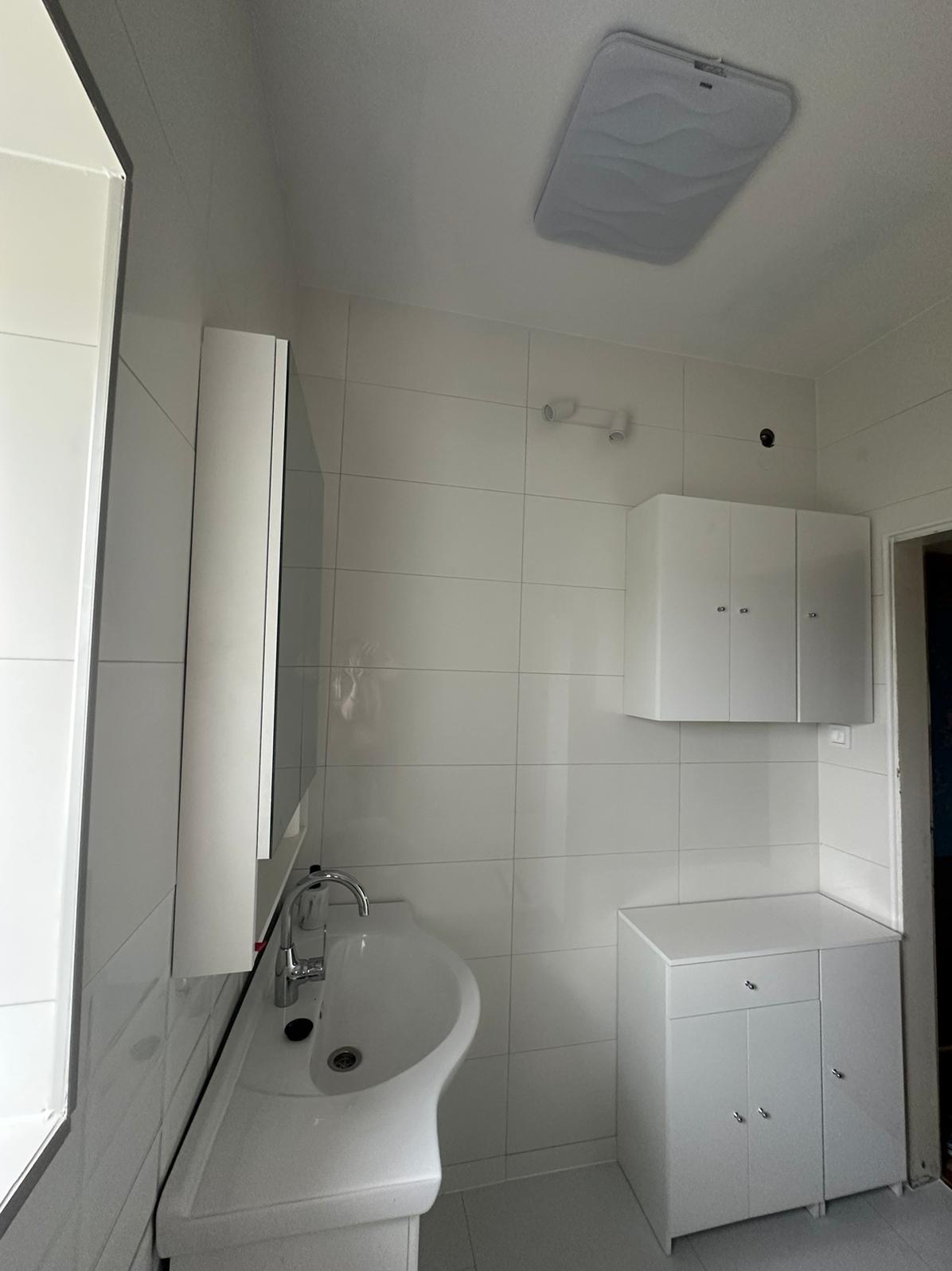 Wyremontowana, minimalistyczna łazienka w bieli z umywalką w kształcie misy, szafką pod umywalką, wiszącą szafką i płytkami ściennymi w regularną siatkę.