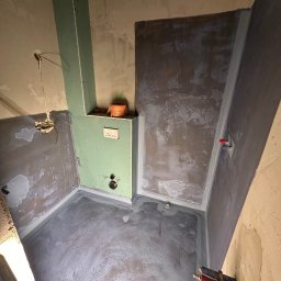 S.A.R.O - Łazienka w trakcie hydroizolacji: ściany i podłoga pokryte szarą warstwą, widoczne rury, zabudowa z płyt gipsowych. Etap prac przed wykończeniem.