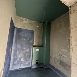 S.A.R.O - Wnętrze łazienki w trakcie prac wykończeniowych: hydroizolacja podłogi, zabudowa stelaża WC płytami GK, surowy mur z betonu komórkowego przy wejściu.