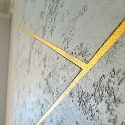 S.A.R.O - Dekoracyjna ściana z szarą fakturą i złotymi, ukośnymi liniami tworzącymi geometryczny wzór. Efektowna aranżacja wnętrza z bliska.