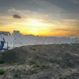 Wznoszenie muru z bloczków betonu komórkowego na fundamencie, dwaj mężczyźni na placu budowy, zachód słońca w tle.