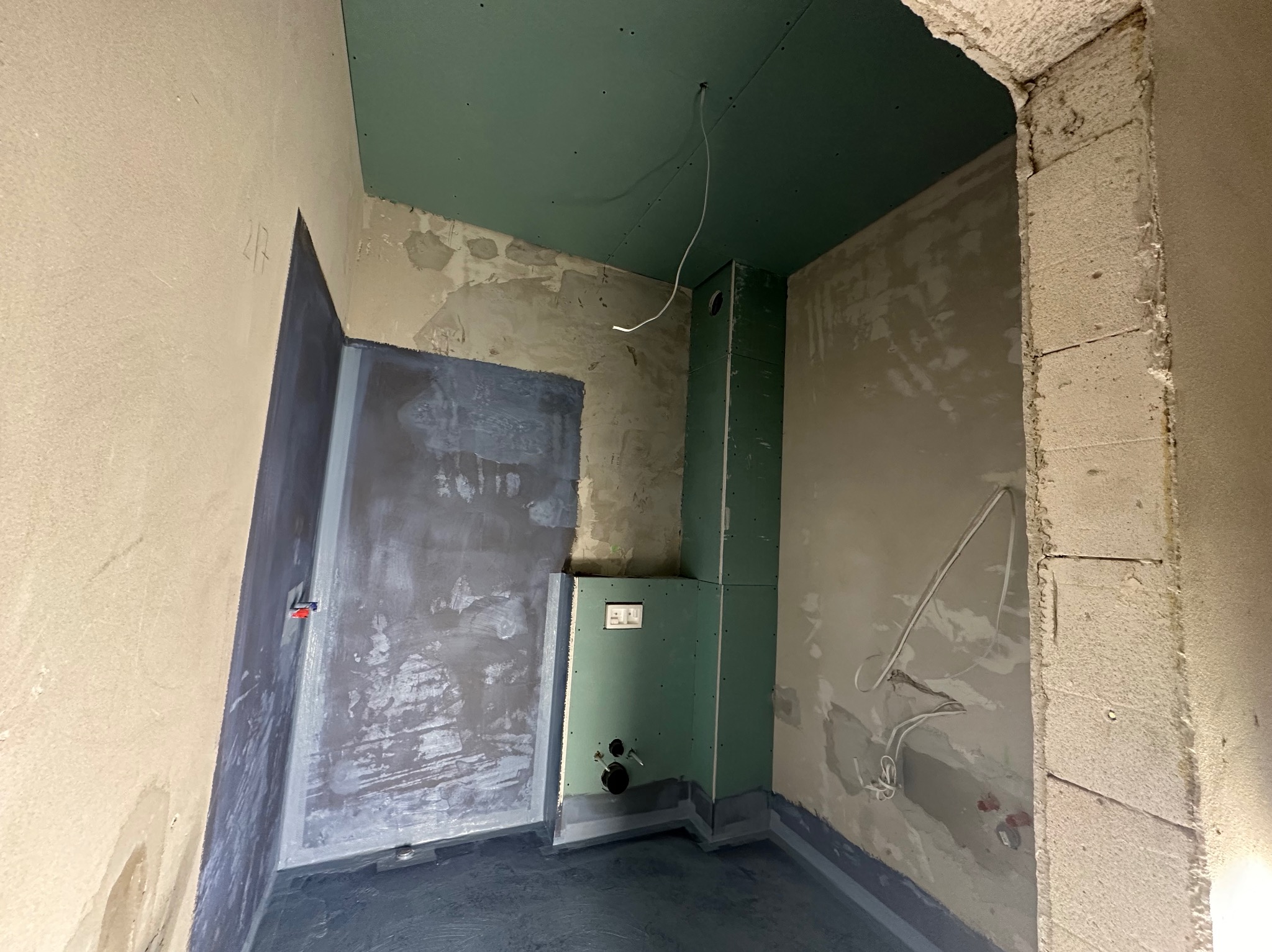 Wnętrze łazienki w trakcie prac wykończeniowych: hydroizolacja podłogi, zabudowa stelaża WC płytami GK, surowy mur z betonu komórkowego przy wejściu.