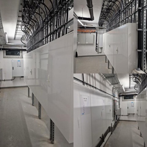 Rząd białych szaf elektrycznych zamontowanych wzdłuż ściany, z widocznymi kablami prowadzonymi w korytach kablowych pod sufitem, w pomieszczeniu technicznym.