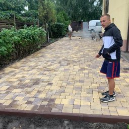 Artem Vynnychuk - Ułożona kostka brukowa w odcieniach beżu i brązu, obrzeża z ciemnobrązowej kostki, osoba w sportowym stroju przygląda się pracy, w tle zaparkowany biały samochód dostawczy oraz druga osoba przy pracy.