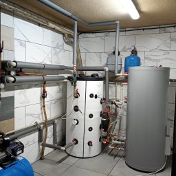 Silesia Energy - Kotłownia z dwoma zbiornikami, rurami w izolacji i białymi płytkami imitującymi marmur na ścianach. Widoczne elementy instalacji grzewczej.