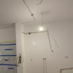 KAMKOP Pałuki Kamil Kopicki - Wnętrze w trakcie remontu z widocznymi przewodami elektrycznymi poprowadzonymi po suficie i ścianach, zabezpieczona folią strefa malarska.