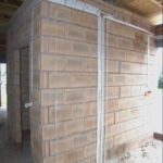 Surowy mur z bloczków betonowych wewnątrz budynku, widoczne białe rury instalacyjne, brak otynkowania, niedokończony etap budowy.