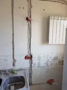 Ściana z wyżłobieniami pod instalację elektryczną i puszkami w Wyrębie, widoczne przewody i fragment zlewu.