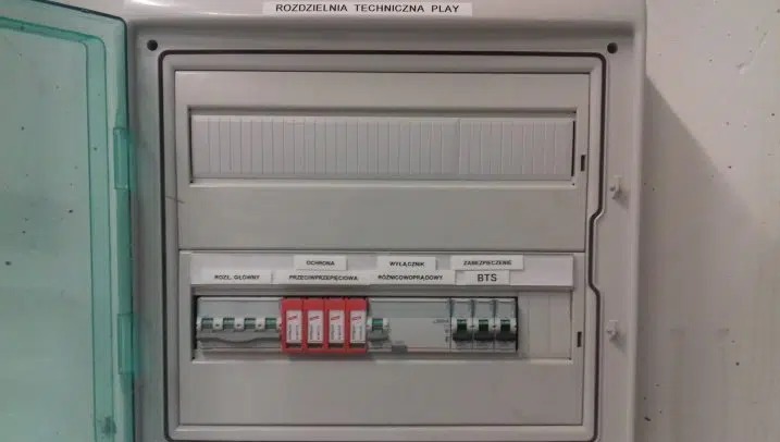 Otwarta skrzynka rozdzielcza 'Rozdzielnia Techniczna Play' z widocznymi bezpiecznikami, wyłącznikami różnicowoprądowymi i zabezpieczeniem BTS.