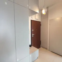 Szara zabudowa meblowa w przedpokoju z drewnianymi drzwiami wejściowymi i nowoczesną lampą wiszącą.