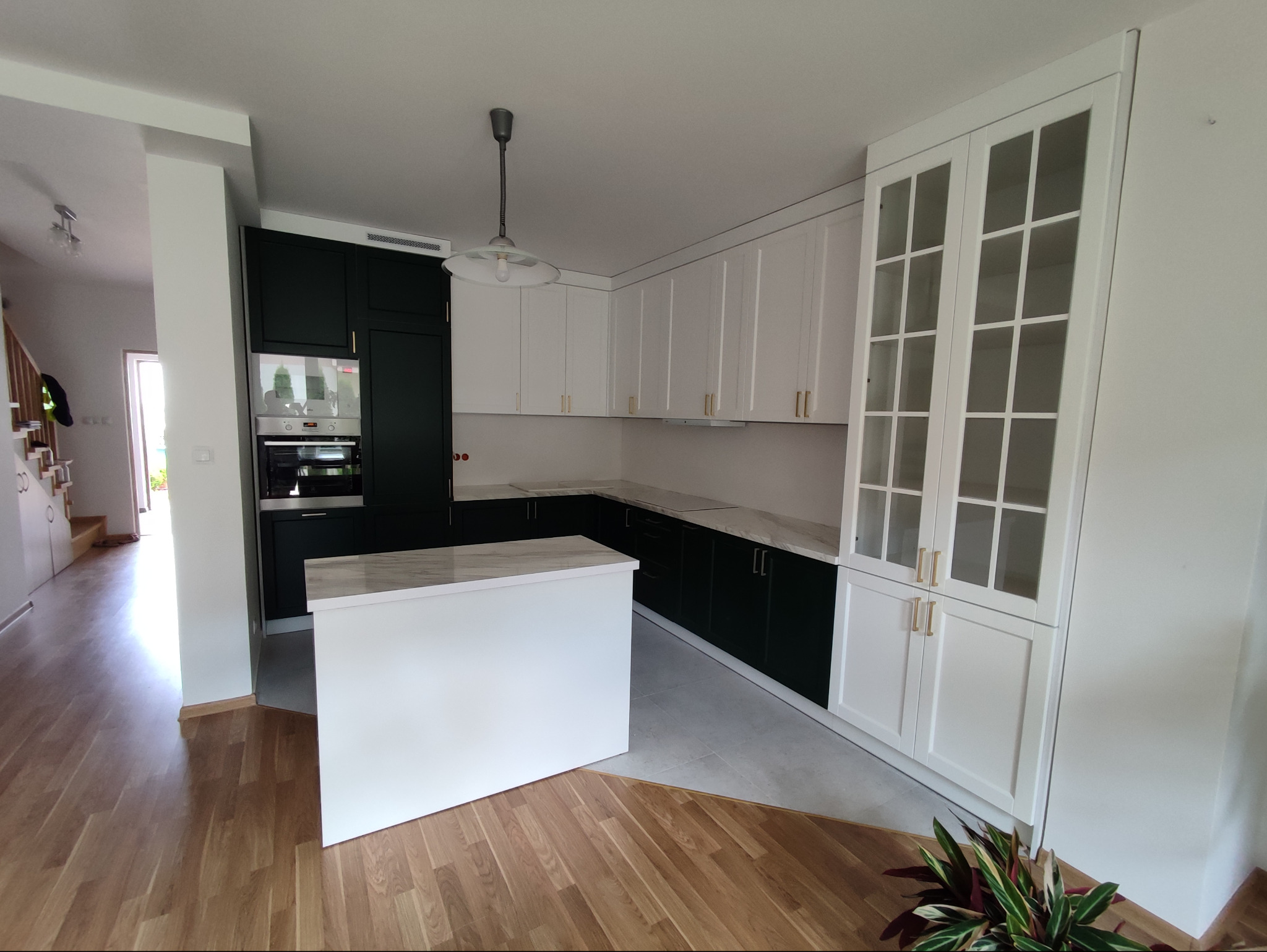 Nowoczesna kuchnia z wyspą, łącząca ciemnozielone dolne szafki z białymi górnymi, marmurowy blat i drewniana podłoga w domu.