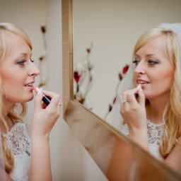 Pro SmArt Studio Adam Kowal - Panna młoda w welonie, aplikująca różową szminkę przed lustrem, widoczne odbicie i pierścionek zaręczynowy.