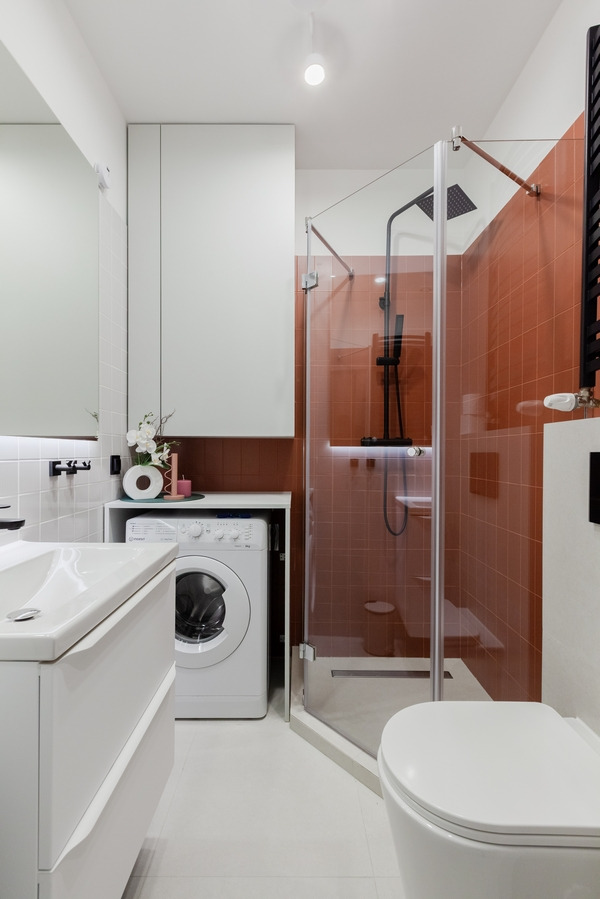 Nowoczesna łazienka z kabiną prysznicową z czarną armaturą, pralką schowaną w zabudowie i białymi meblami.