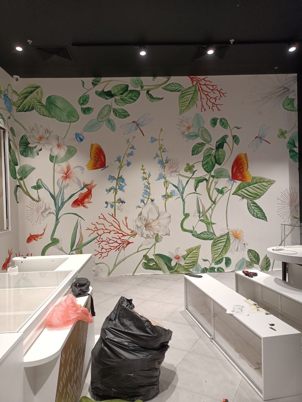 Montaż fototapety z motywem florystycznym w lokalu usługowym w Grabicy, widoczny worek na śmieci i narzędzia pracy.