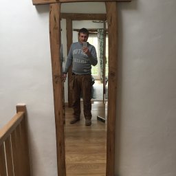 Woodworking - Mężczyzna w odblasku lustra z drewnianą ramą, stojącego na drewnianych schodach, widoczny poziomica i narzędzia w pasie.