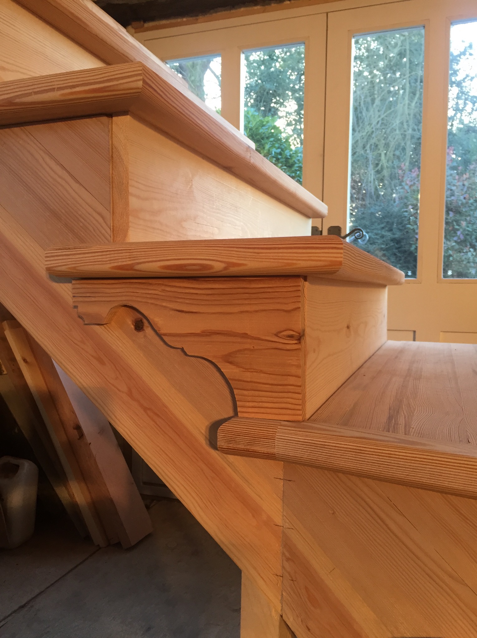 Detal drewnianych schodów z widocznym ozdobnym wykończeniem stopnia i fragmentem okna w tle.