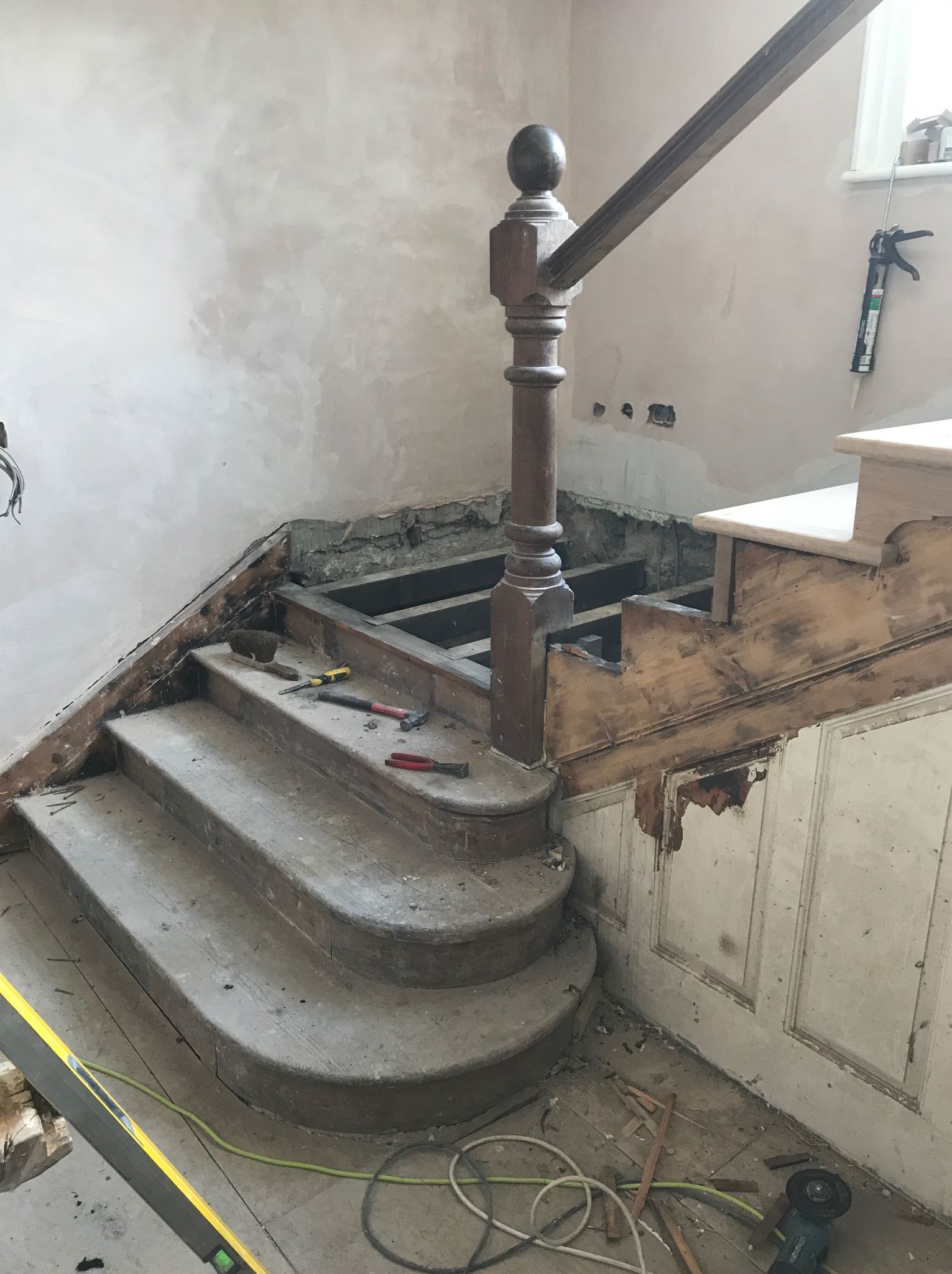 Demontaż drewnianych schodów z balustradą, widoczne narzędzia i elementy konstrukcyjne, ściany w trakcie remontu.