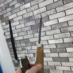 Remont Szczecin - Wykończona ściana z dekoracyjnej cegły w odcieniach beżu i brązu, z narzędziami glazurniczymi w dłoni, sugerującymi etap fugowania. Detal wykończenia wnętrza.