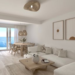 tin design - Jasne wnętrze z widokiem na morze: biała sofa, drewniany stół z krzesłami, minimalistyczne obrazy na ścianie. Naturalne materiały i spokojna kolorystyka.
