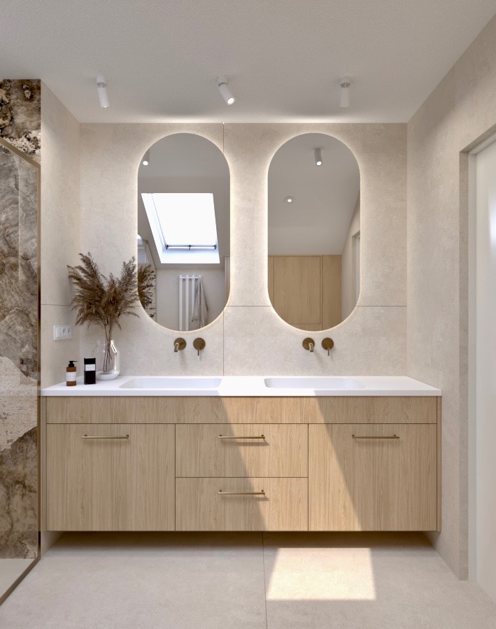 Jasna łazienka z dwoma owalnymi lustrami z podświetleniem LED, drewnianą szafką pod umywalką i marmurową ścianą prysznica po lewej stronie.