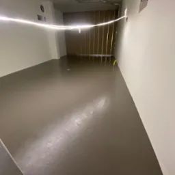 Gładka, brązowa wylewka samopoziomująca w jasnym pomieszczeniu, widoczne żółte znaczniki poziomu i metalowa konstrukcja ściany w tle.