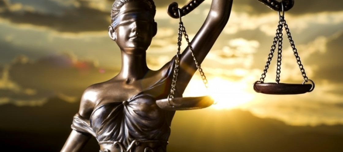 Statua Temidy z zasłoniętymi oczami, trzymająca wagę na tle zachodzącego słońca i chmur.