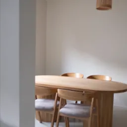 Minimalistyczna jadalnia z owalnym, jasnym stołem z drewna i krzesłami z szarymi siedziskami, oświetlona plecioną lampą wiszącą, widok zza rogu ściany.