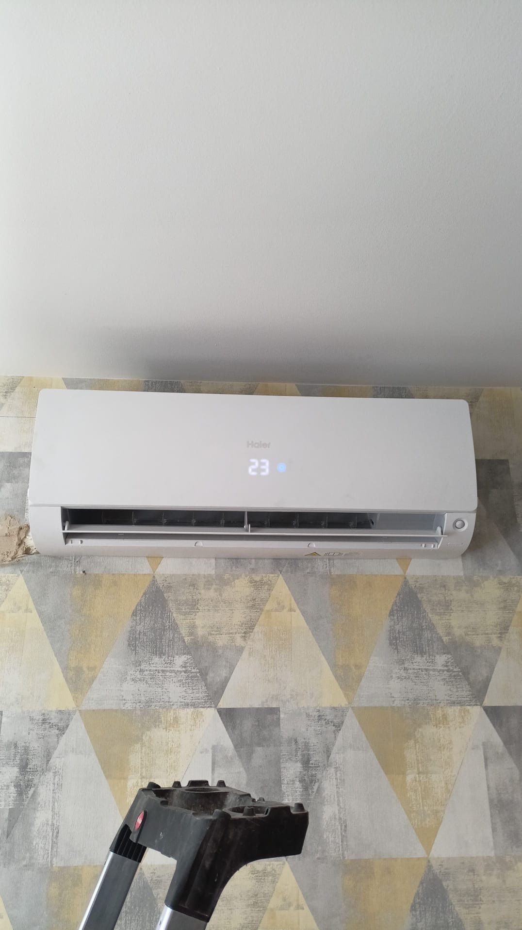 Zamontowana biała klimatyzacja Haier z wyświetlaczem 23°C na ścianie w geometryczne wzory w Poznaniu. Widoczny fragment drabiny.