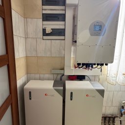 SKENERGY SPÓŁKA Z OGRANICZONĄ ODPOWIEDZIALNOŚCIĄ - Domowa instalacja: dwa magazyny energii Felicitysolar obok inwertera Deye, z widoczną skrzynką bezpiecznikową na ścianie z beżowych płytek. Estetyczne rozwiązanie.