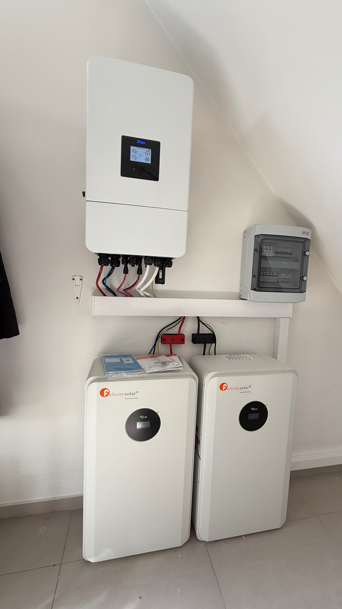 Instalacja magazynu energii Felicity Solar z inwerterem Deye i skrzynką bezpiecznikową na białej ścianie. Widoczne kable i dokumentacja.