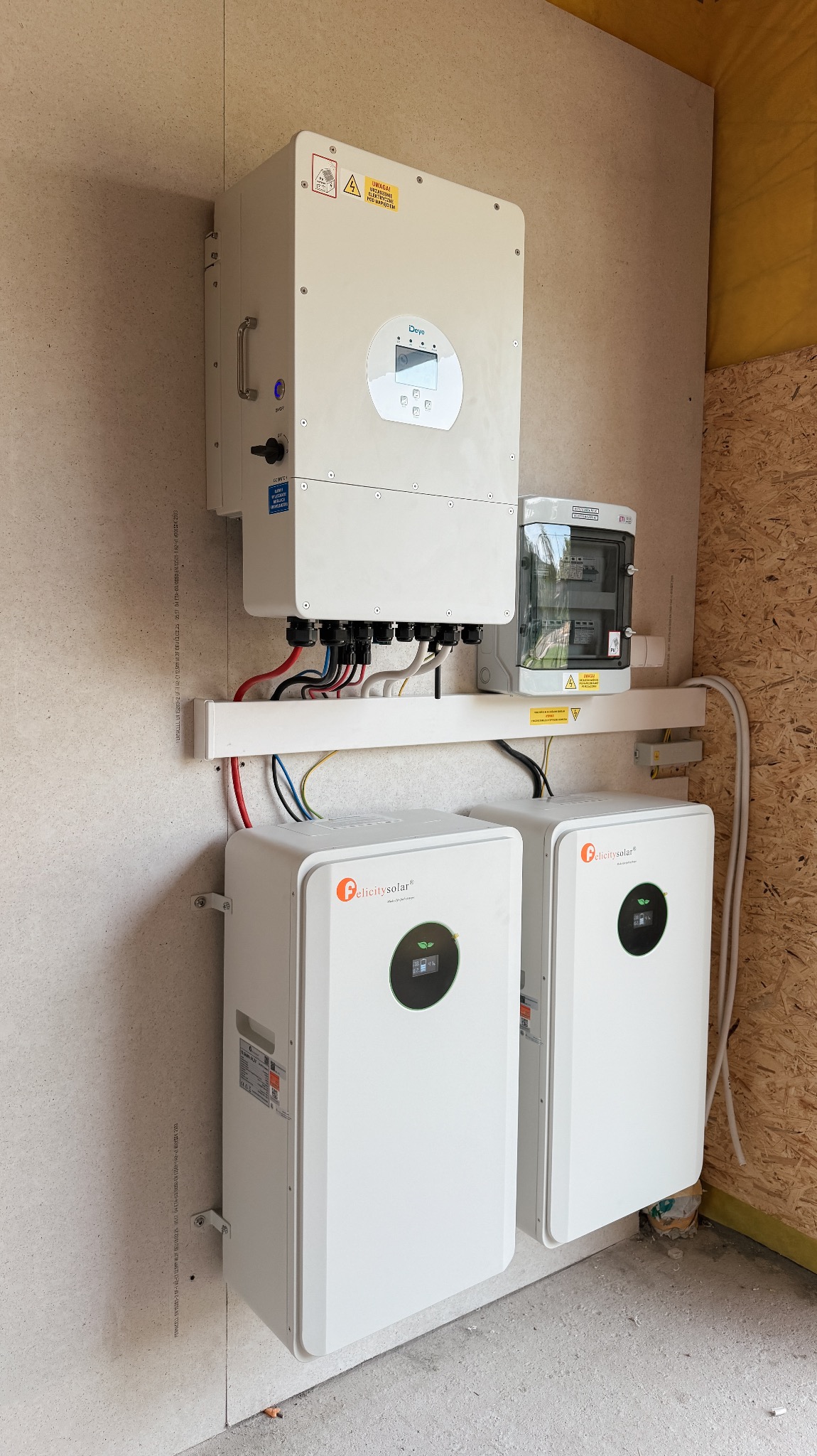 Zestaw urządzeń fotowoltaicznych marki Felicitysolar i Deye zamontowany na ścianie z płyt OSB. Widoczny inwerter, magazyny energii i skrzynka zabezpieczeń.