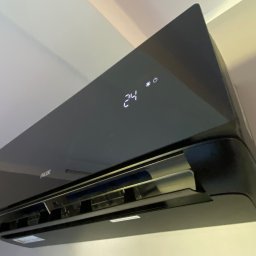 FL-System Grzegorz Górski - Czarny klimatyzator AUX na ścianie, wyświetlający temperaturę 24 stopnie Celsjusza, widok od dołu.