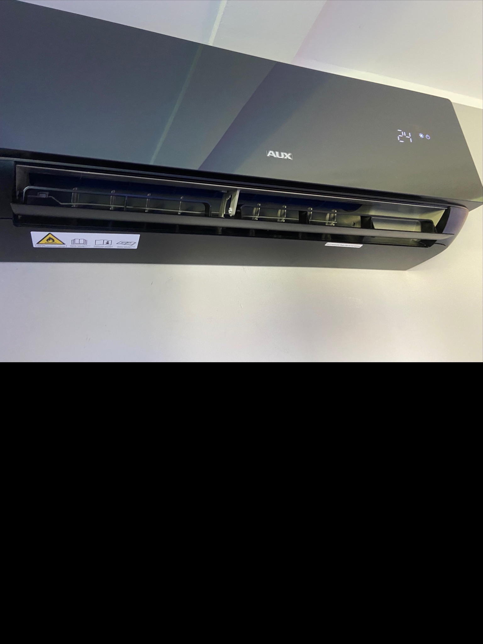 Czarny klimatyzator marki AUX zamontowany na białej ścianie, wyświetlający temperaturę 24 stopnie Celsjusza.