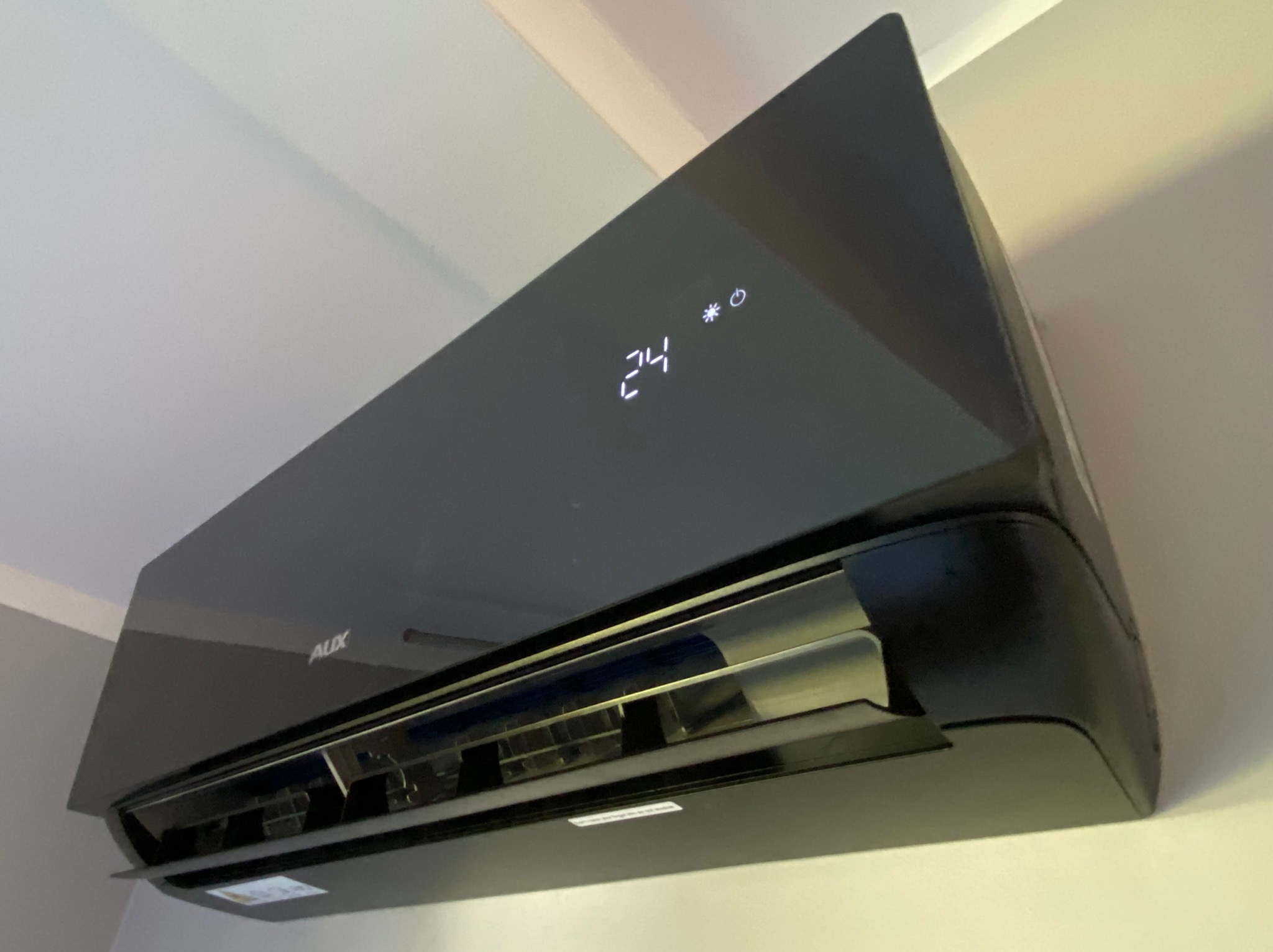 Czarny klimatyzator AUX na ścianie, wyświetlający temperaturę 24 stopnie Celsjusza, widok od dołu.