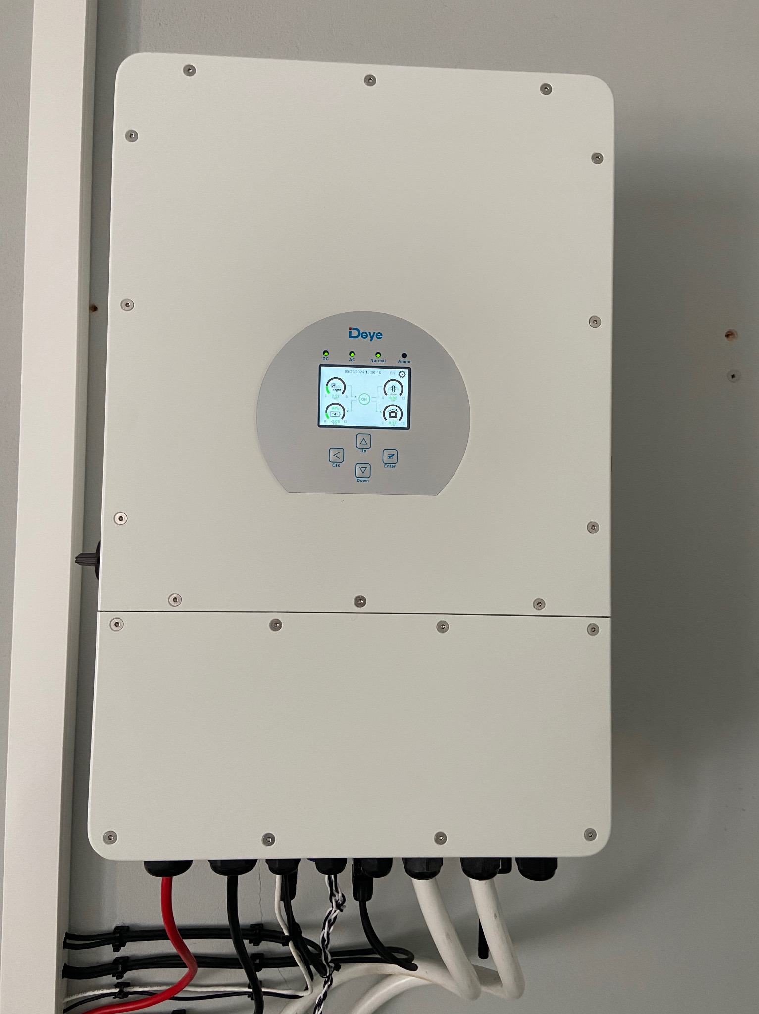 Biały inwerter Deye na ścianie z podłączonymi kablami. Widoczny wyświetlacz z parametrami pracy. Instalacja wewnątrz budynku.