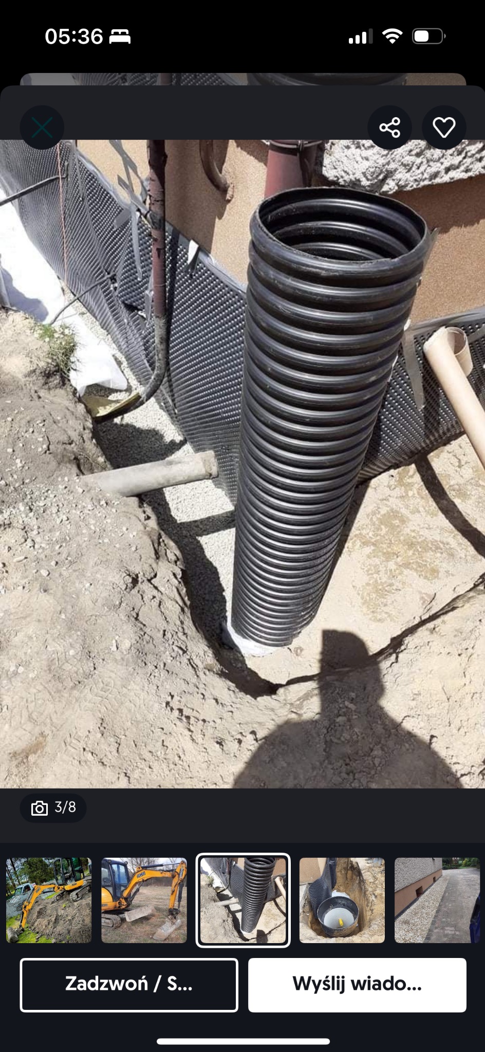 Czarna, karbowana rura pionowa w wykopie, obok ściany fundamentowej z izolacją kubełkową i drenażem obsypanym żwirem.