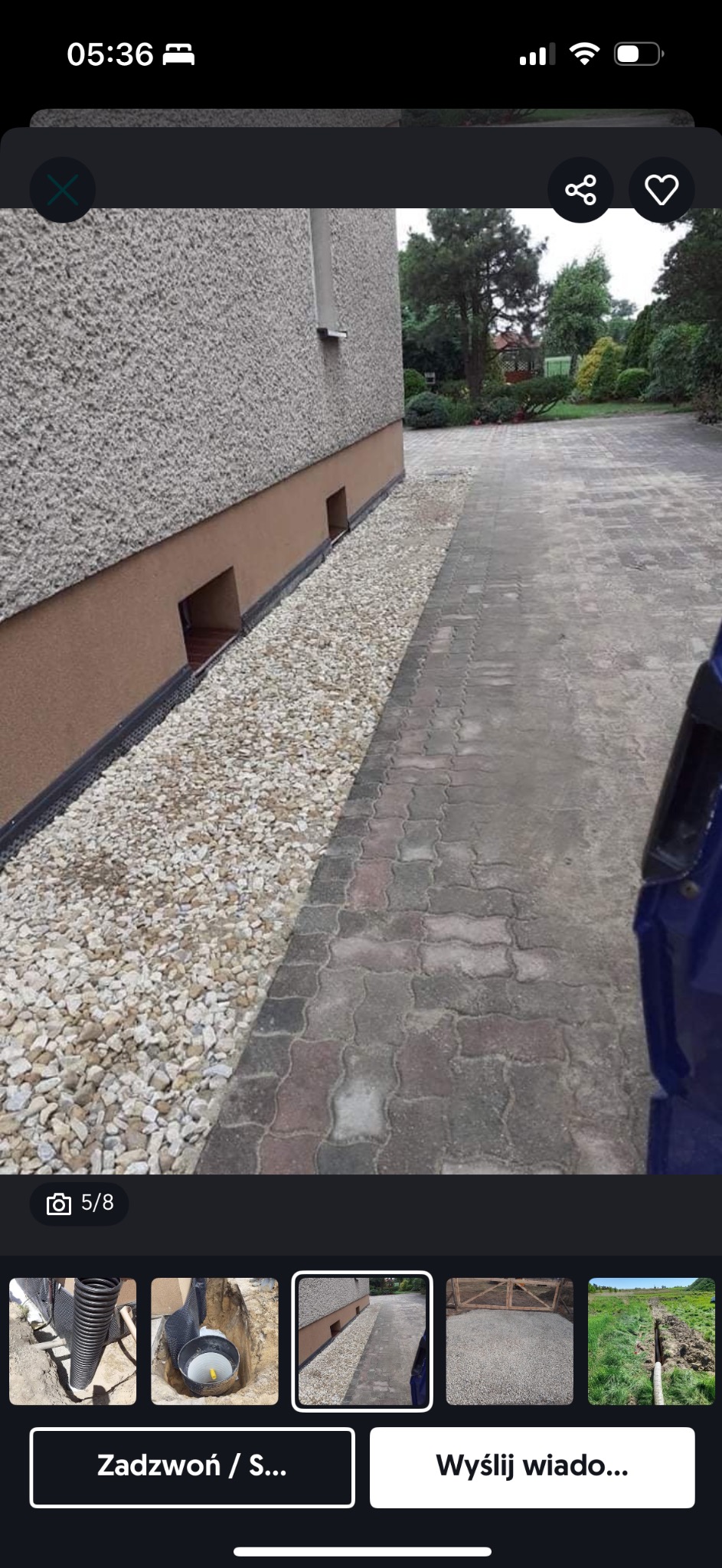 Odprowadzenie wody opaską żwirową przy ścianie budynku z widocznymi otworami wentylacyjnymi w fundamencie i brukowanym chodnikiem