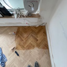 Done and Dusted - Parkiet w jodełkę częściowo polakierowany, widoczny pędzel, wałek i stopy osoby filmującej. Na parapecie płyta winylowa i przedłużacz. Ściana częściowo pomalowana.