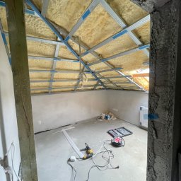 DONE AND DUSTED KONRAD SZEWCZYK - Poddasze w trakcie prac: ocieplona pianką PUR skośna część dachu z metalową konstrukcją pod płyty g-k. Na podłodze narzędzia i akcesoria budowlane.