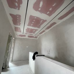 Done and Dusted - Sufit z płyt karton-gips, częściowo zaszpachlowany, z czarnymi listwami. Ściany przygotowane do malowania. Widoczne kable.