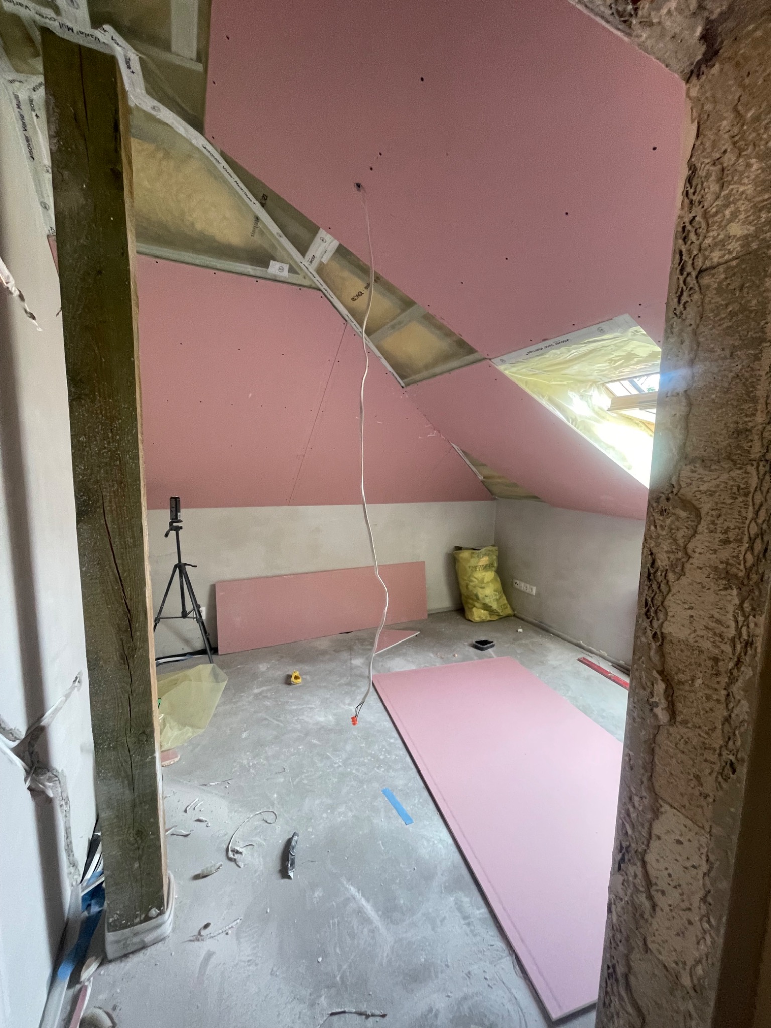 Montaż różowych płyt gipsowo-kartonowych na poddaszu w Skarżysko-Kamienna. Widoczne izolacje i elementy konstrukcyjne dachu, sufitu. Prace wykończeniowe w trakcie.