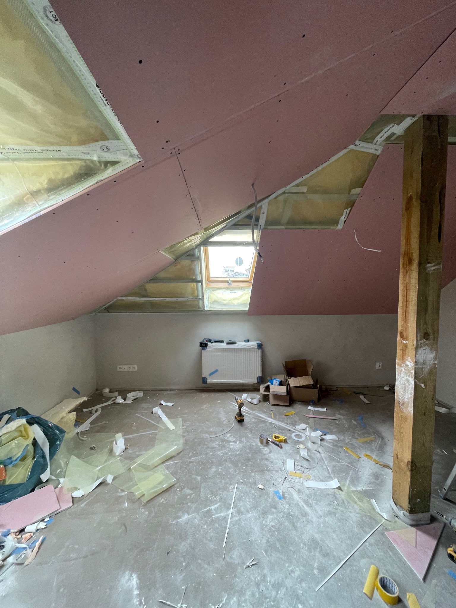 Poddasze w trakcie prac wykończeniowych: montaż płyt kartonowo-gipsowych na skośnym dachu, widoczne ocieplenie, okno dachowe i narzędzia pracy.