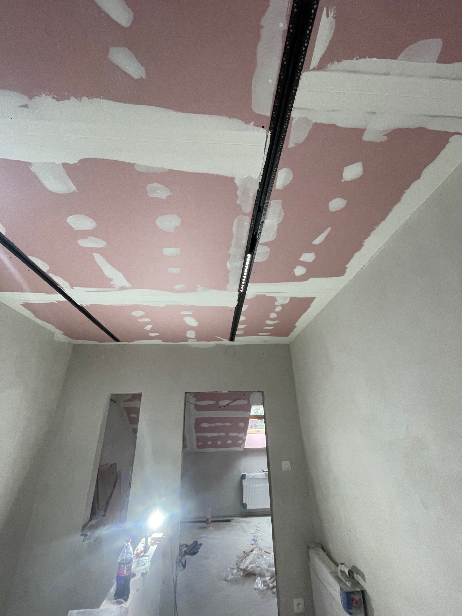 Montaż płyt gipsowo-kartonowych na suficie z widocznymi profilami i wstępnie zaszpachlowanymi łączeniami. Prace wykończeniowe w trakcie realizacji.