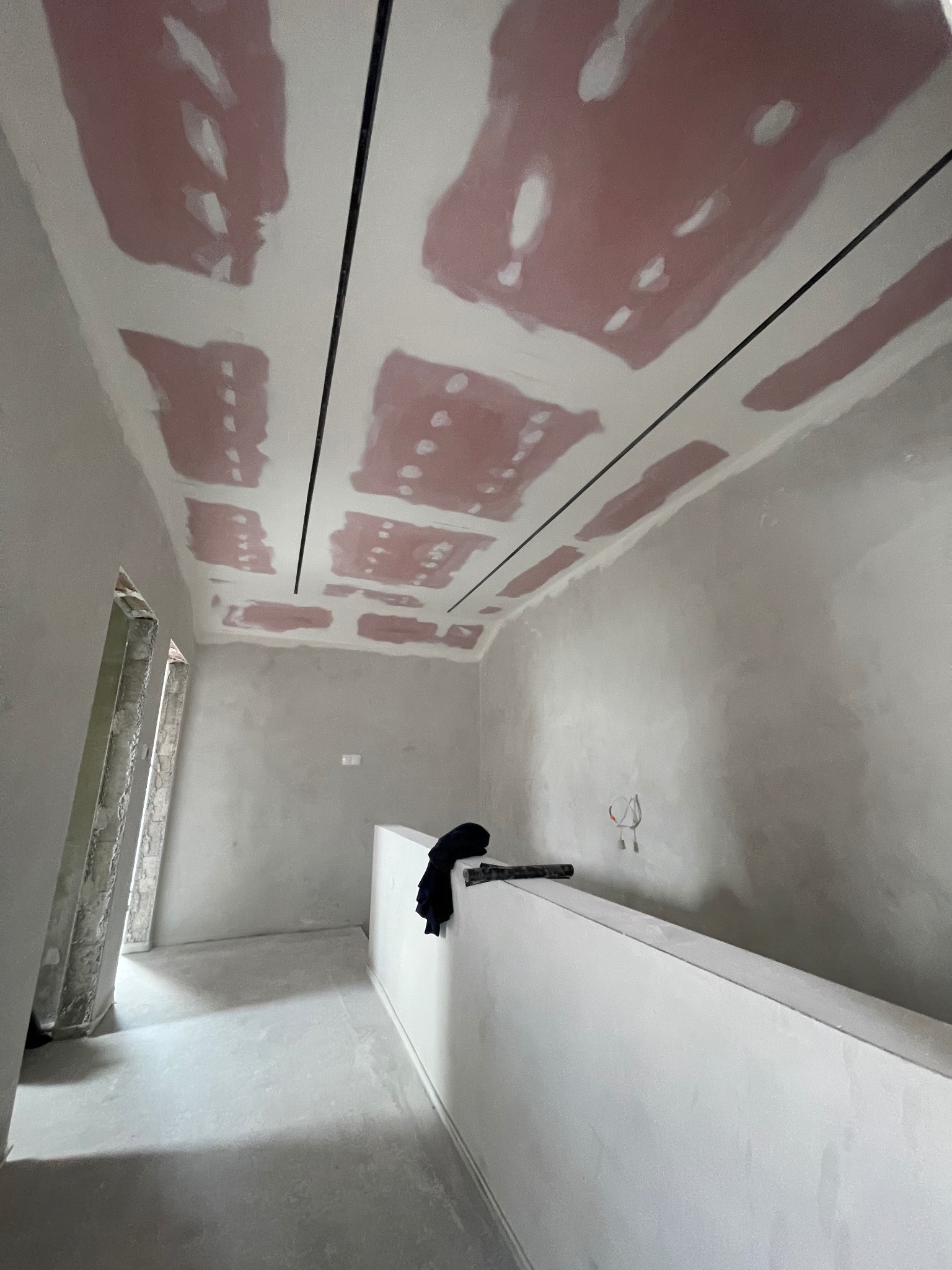 Sufit z płyt karton-gips, częściowo zaszpachlowany, z czarnymi listwami. Ściany przygotowane do malowania. Widoczne kable.